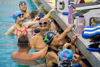 Group of masters swimmers at edge of pool smiling at each other.